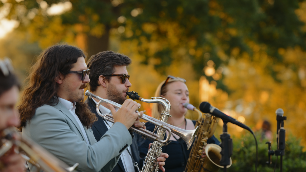 brass band playing outside the The Little Green Wedding Barn at golden hour captured by a Norfolk wedding videographer