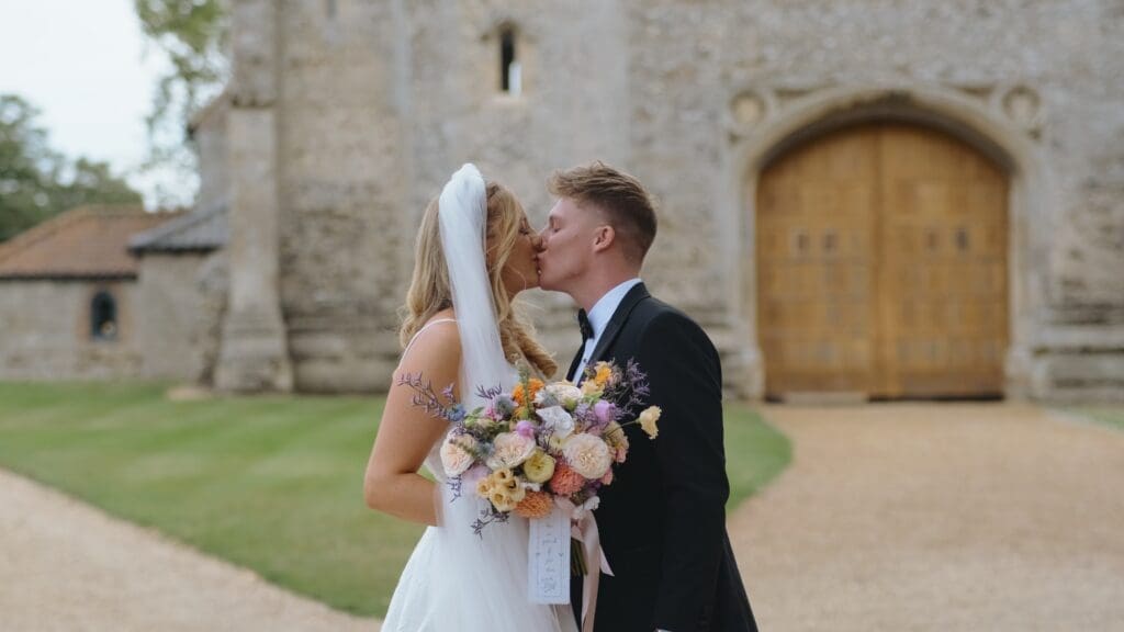 Bride and groom share a kiss outside Pentney Abbey gates