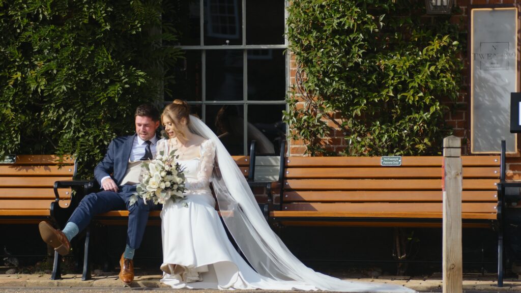 Bride and groom sitting on a bench in burnham market in Norfolk on their wedding day